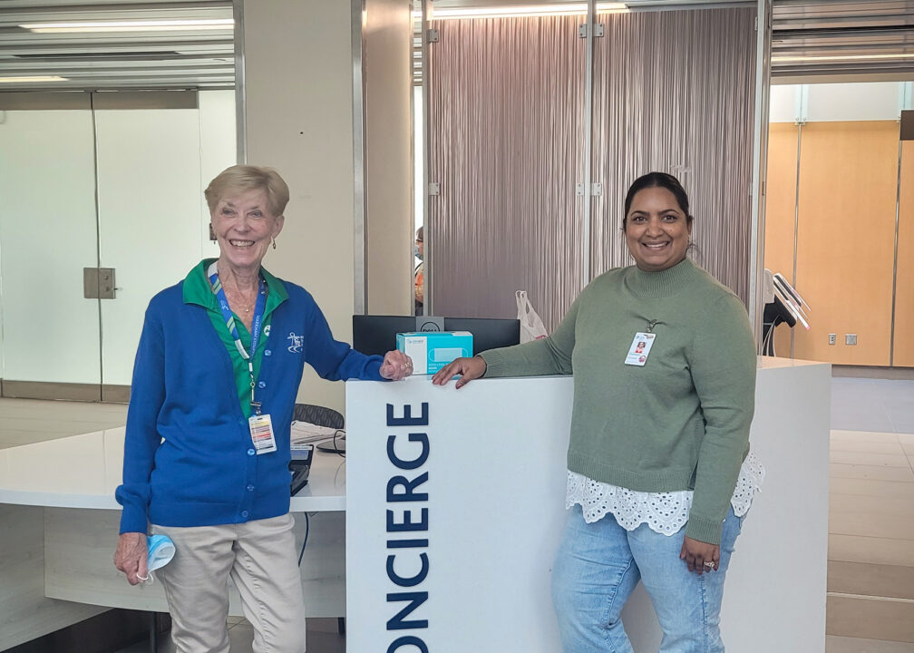 Two hospital volunteers stand beside the concierge desk inside the main entrance at Markham Stouffville Hospital.