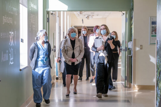 A group of women wearing masks talk amongst each other as they walk down a hallway inside the hospital.