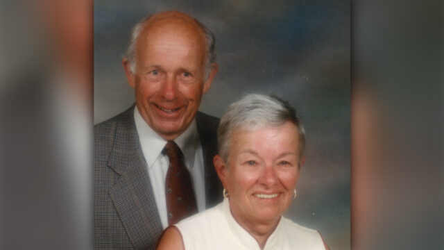 Portrait style photo of John and Patricia McCutcheon, John wearing a suit and Patricia a white shirt in front of a grey backdrop.