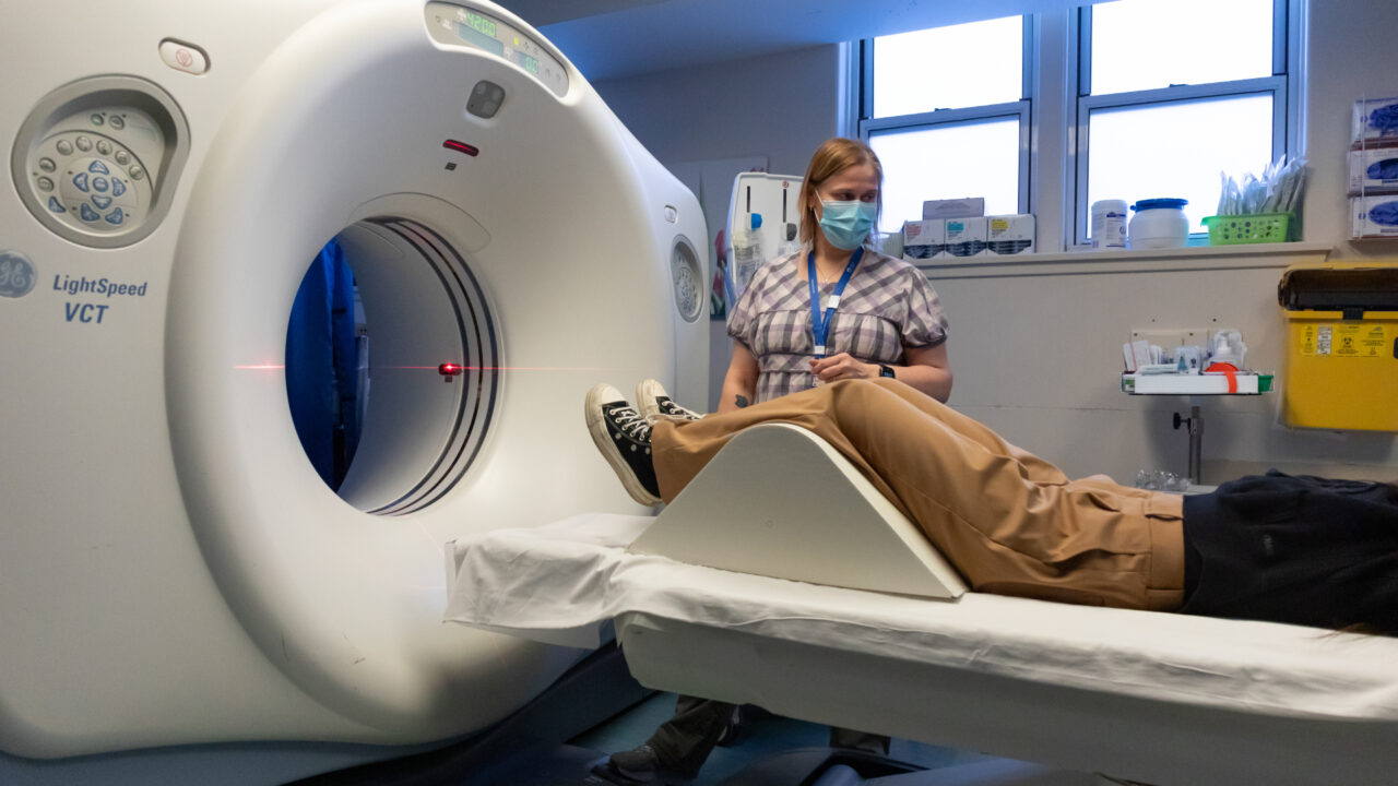 A patient prepares for a diagnostic imaging procedure as a staff member looks on