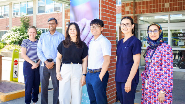 A group of staff stand outside the main entrance of Uxbridge Hospital, including the two new family medicine residents.