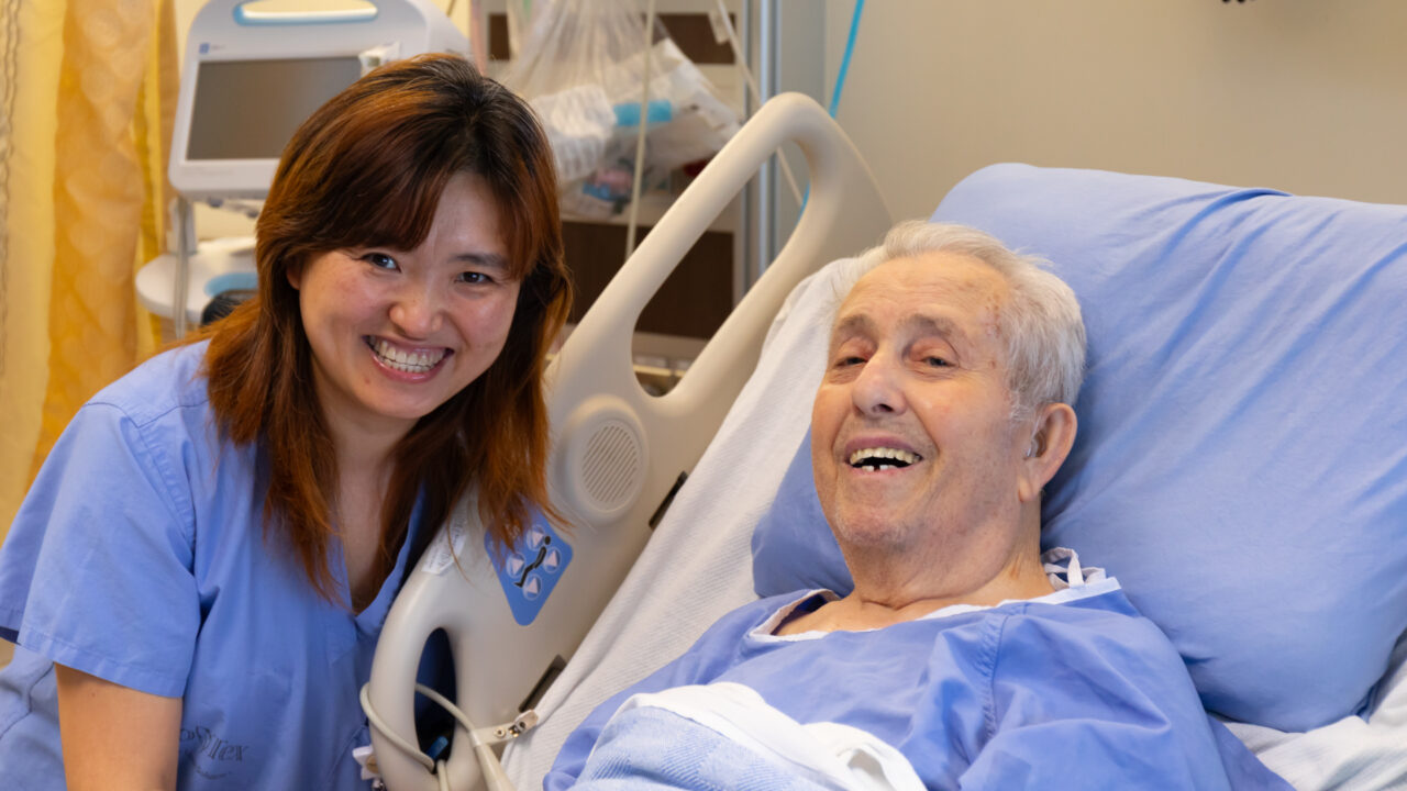 A staff member sits next to the bedside of a patient