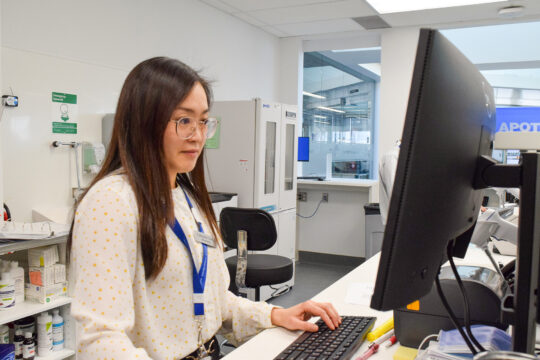 A staff member in pharmacy reviews details on a computer screen.